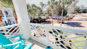 A wooden deck with turquoise chairs, a white railing, and a view of a street with palm trees and a white car. - Million dollar villa · Beachfront neighborhood · Free cruise · Resort amenities (Destin)