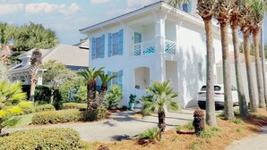 A white building with blue shutters, surrounded by palm trees and a well-maintained garden. - Million dollar villa · Beachfront neighborhood · Free cruise · Resort amenities (Destin)