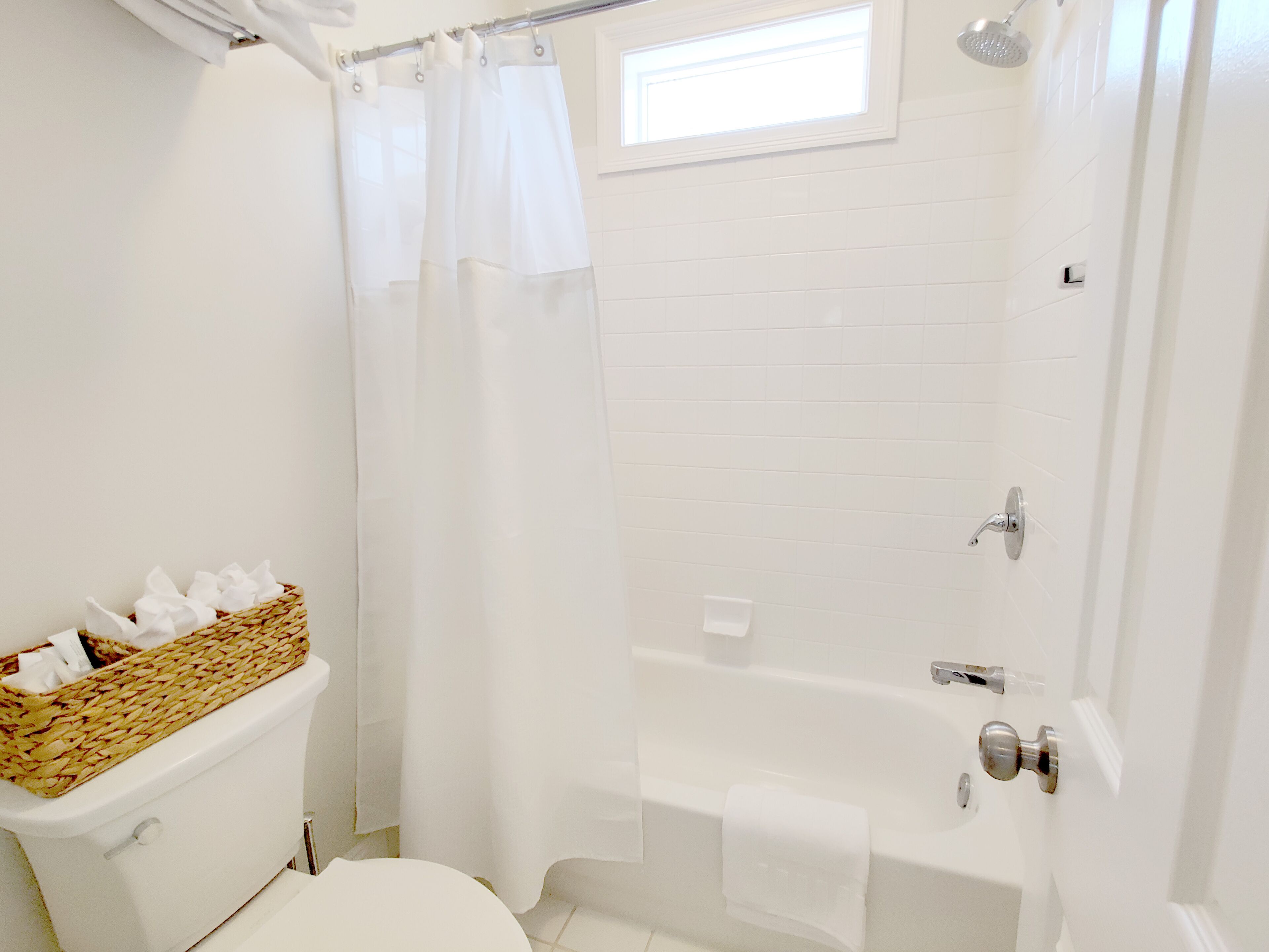 A bathroom with a toilet, a shower with a glass door, and a window above the shower.