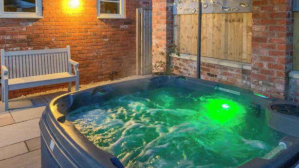 A hot tub with a green light, a bench, and a brick wall with windows. - 2 bedroom accommodation in Swanwick (Swanwick)
