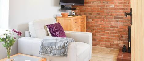 Una sala de estar moderna con un sofá blanco, una pequeña mesita de madera, un televisor de pantalla plana montado en una pared de ladrillo y una chimenea.