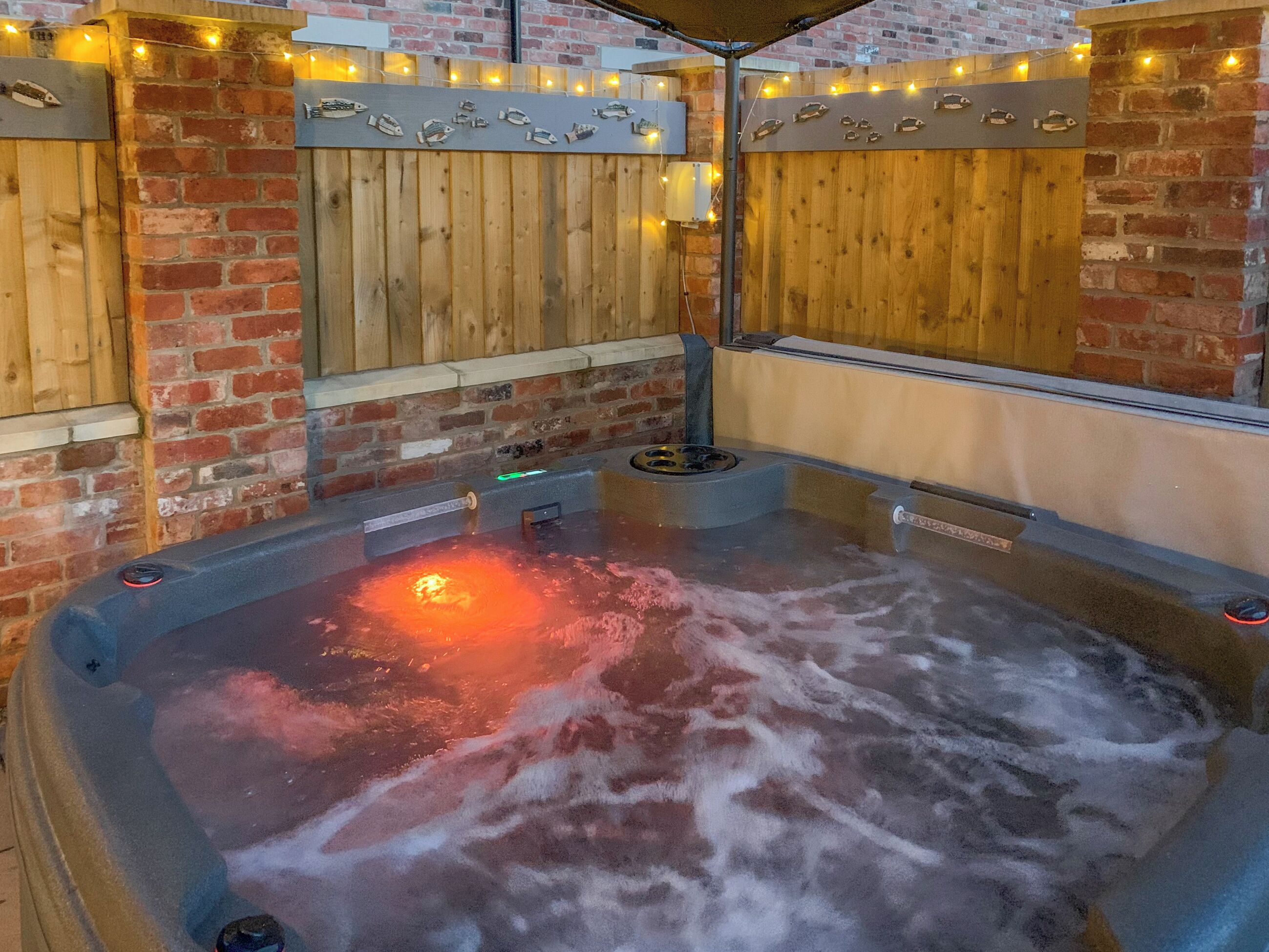 Een hottubgedeelte met houten wanden en bakstenen accenten, omringd door lichtslingers.
