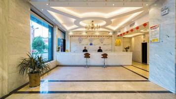 A hotel lobby with a marble reception desk, two bar stools, a chandelier, and red lanterns.