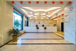 Un hall d’hôtel avec un comptoir de réception en marbre, deux tabourets de bar, un lustre et des lanternes rouges.