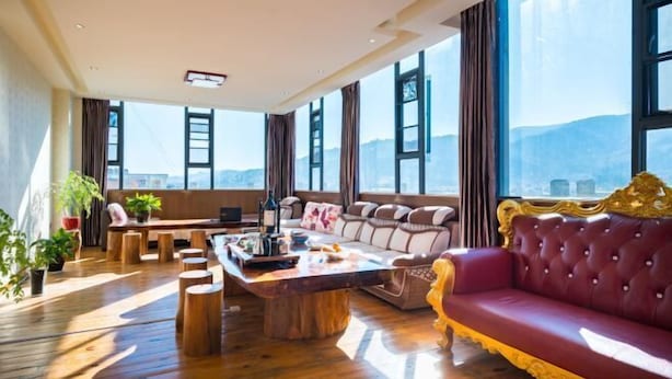 Un salón amplio con suelo de madera, un sofá rojo, una mesa de centro de madera y vistas a montañas a través de amplios ventanales.