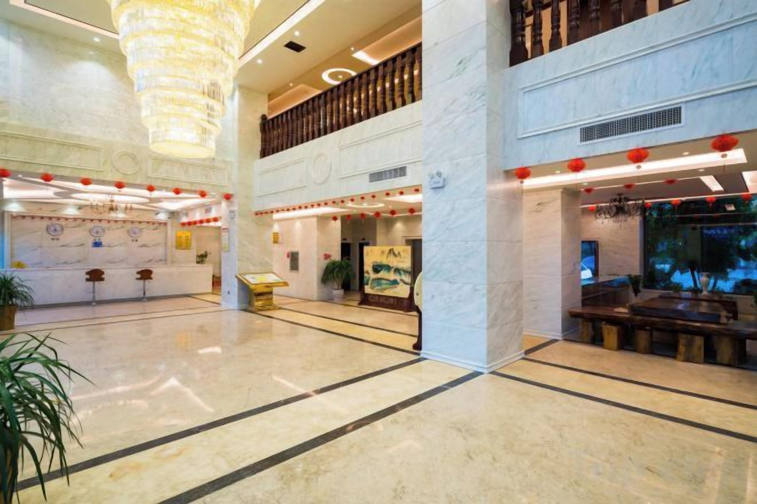 A spacious lobby with a high ceiling, marble flooring, and a large chandelier. There are seating areas and a reception desk.