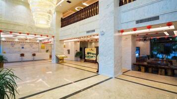 A spacious lobby with a high ceiling, marble flooring, and a large chandelier. There are seating areas and a reception desk.