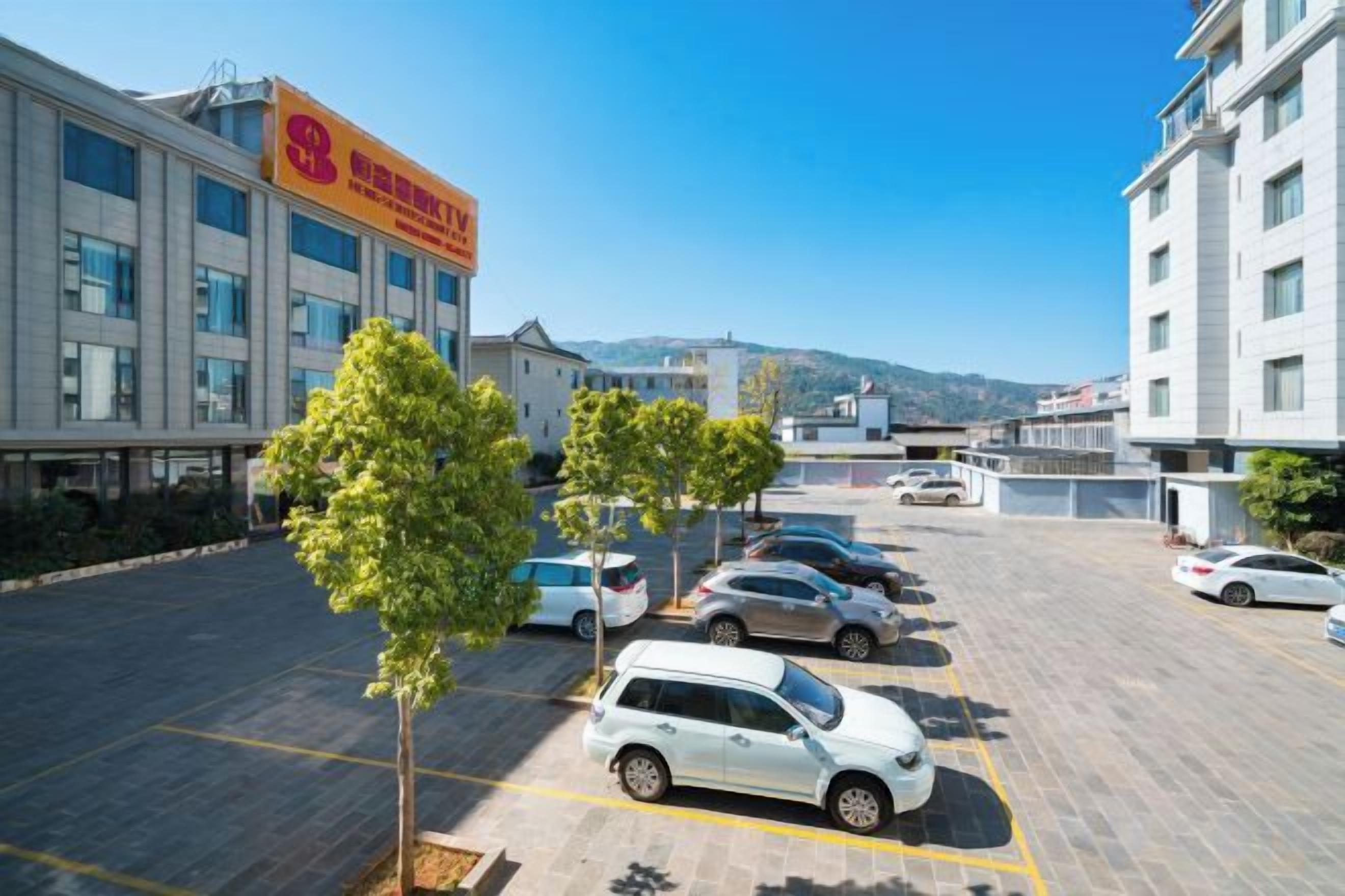 Un parking avec plusieurs voitures, un bâtiment portant une enseigne et un ciel dégagé.