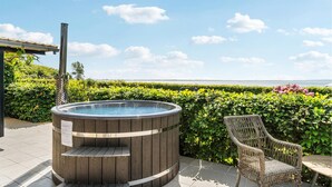 A hot tub with a wooden exterior, a wicker chair, and a hedge in the background. - Gorgeous home in øster assels (Øster Assels)