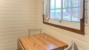 A corner room with a wooden table and two chairs, a window with a view of houses, and a white curtain. - Nice home in Offersøy with sauna (Offersøy)