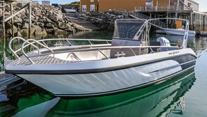 A small, white motorboat docked at a marina with a rocky shoreline and a wooden building in the background. - Nice home in Offersøy with sauna (Offersøy)