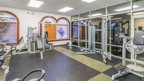 Ett gym med olika typer av träningsutrustning, stora fönster och ett rutmönstrat golv.