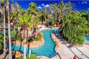A swimming pool surrounded by palm trees and tropical plants, with lounge chairs and a water slide. - 4 bdrm townhouse - 2 king size bdrm suites; next to pool, lazy river and Disney! (Davenport)