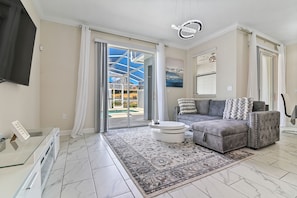 A modern living room with a grey sectional sofa, a round coffee table, and a large glass door leading to an outdoor area. - Your Dream Vacation - Brand New Resort Home! (Four Corners)