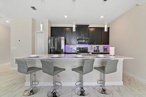 A modern kitchen with a central island, stainless steel appliances, and bar stools. - Your Dream Vacation - Brand New Resort Home! (Four Corners)