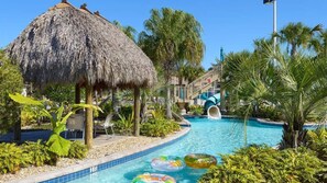 A pool area with a thatched-roof structure, palm trees, and a water slide. - Your Dream Vacation - Brand New Resort Home! (Four Corners)