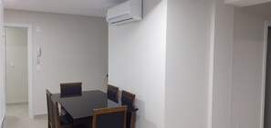 A dining area with a table and chairs, an air conditioning unit mounted on the wall, and a door leading to another room.