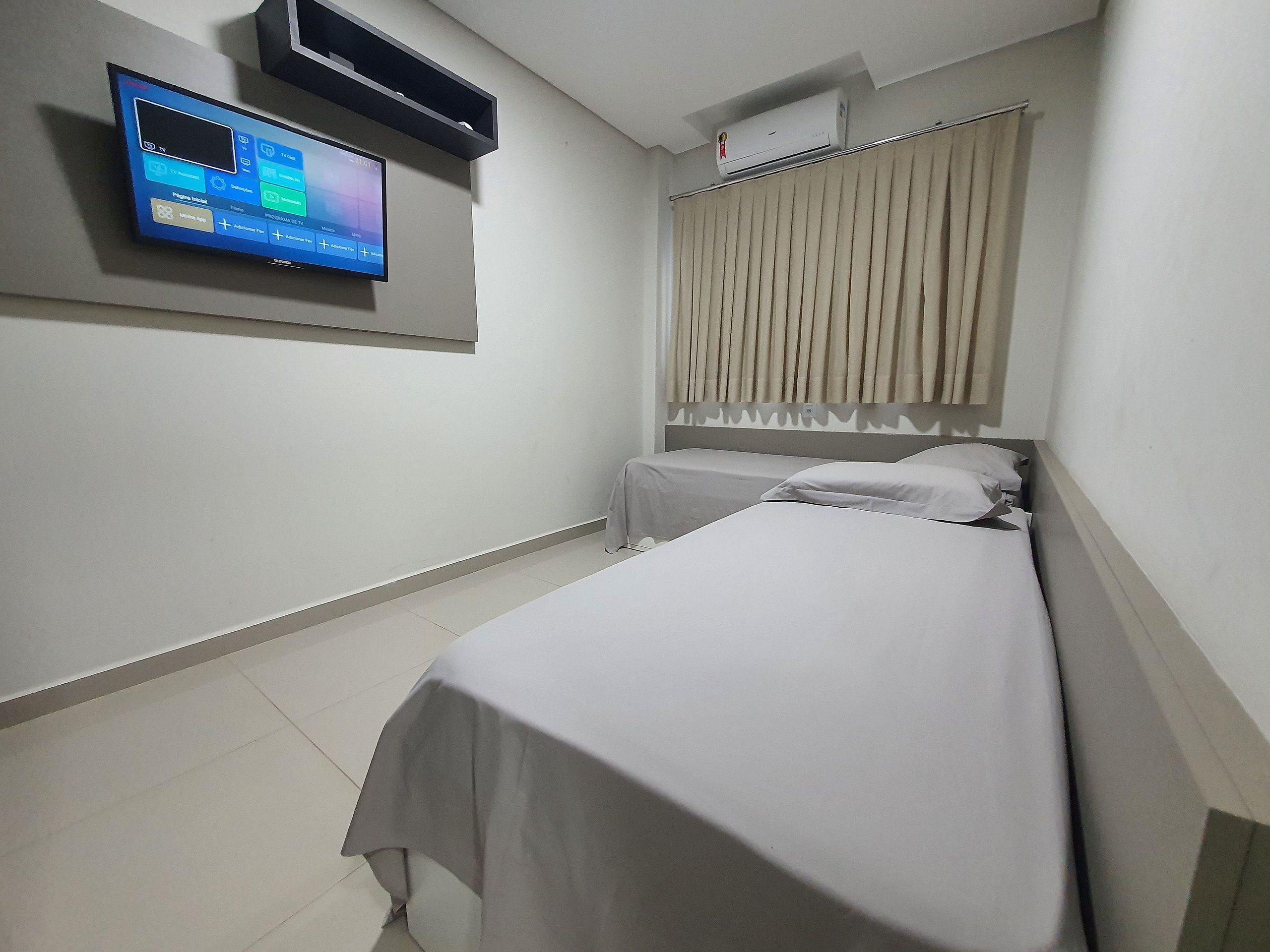 A hotel room with two beds, a TV mounted on the wall, and an air conditioning unit above the window.