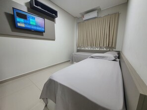 Habitación de hotel con dos camas, un televisor montado en la pared y un equipo de aire acondicionado sobre la ventana.
