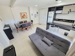 Un apartamento moderno con un sofá gris, una zona de comedor con una mesa y sillas, una cocina con microondas y un cuadro en la pared.