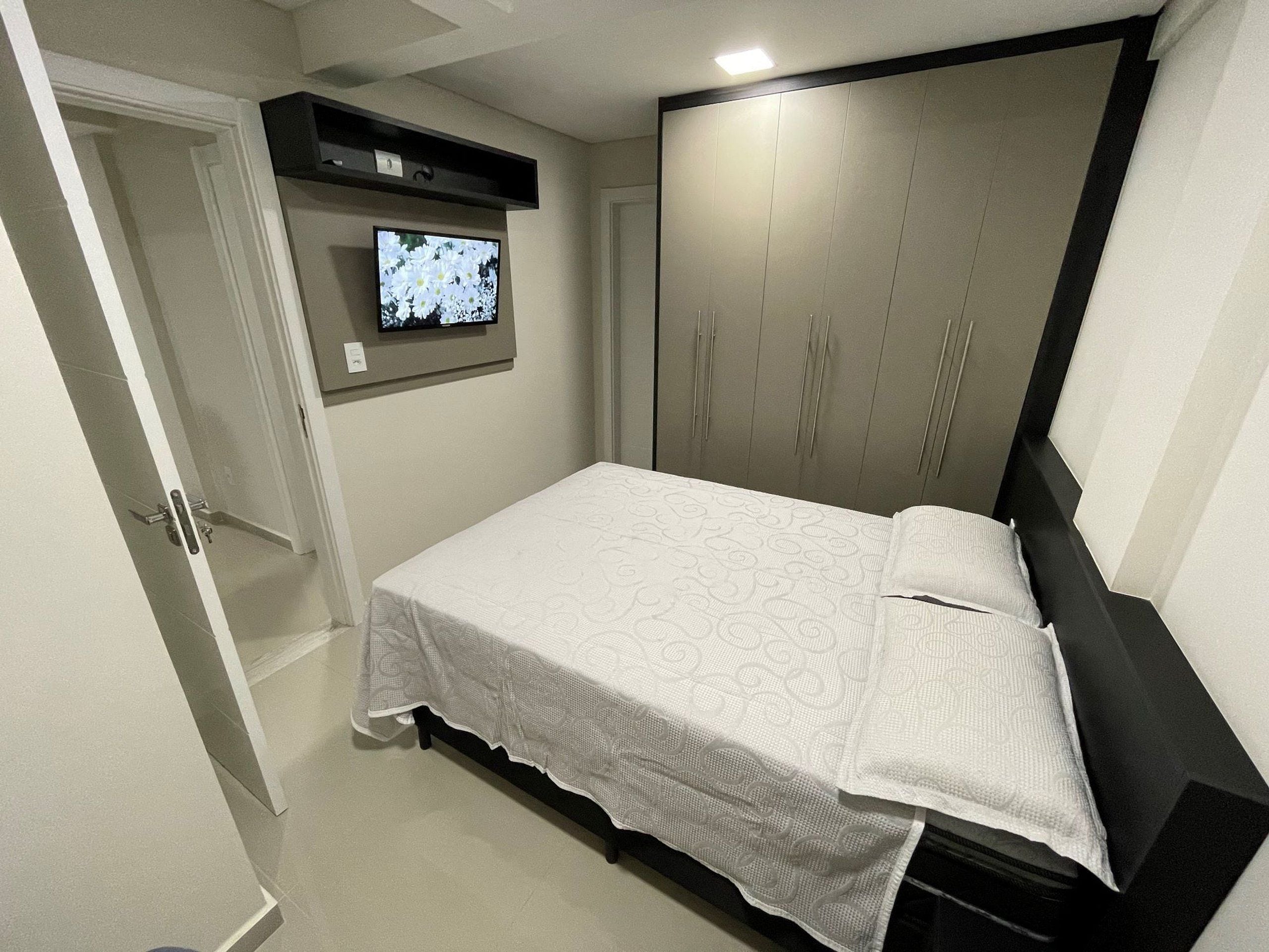 Quarto com cama, televisão na parede e guarda-roupa.