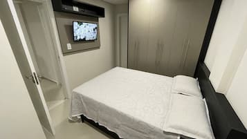 Quarto com cama, televisão na parede e guarda-roupa.