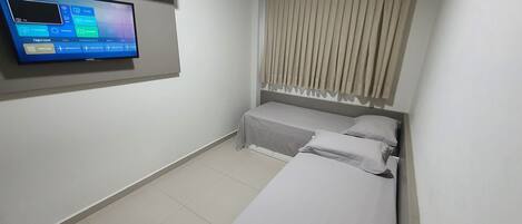 A hotel room with a bed, a TV mounted on the wall, and a window with curtains.