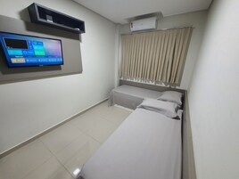 Una habitación de hotel con cama, televisor montado en la pared y ventana con cortinas.