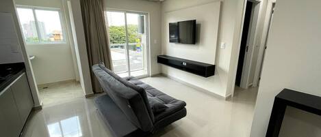 A modern living room with a sofa, a flat-screen TV, and a sliding door leading to a balcony.