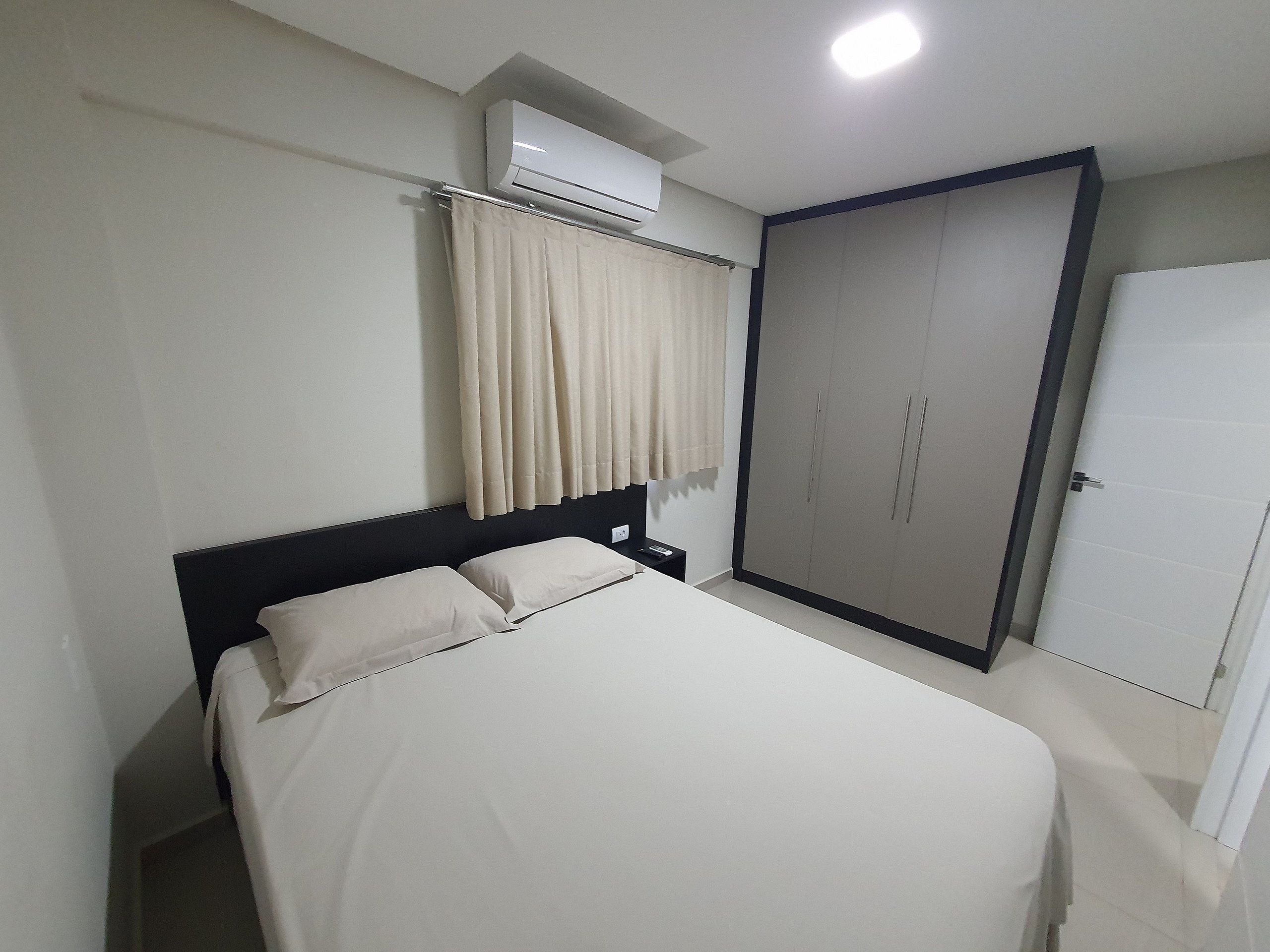 A bedroom with a bed, a wardrobe, an air conditioning unit, and a curtain.