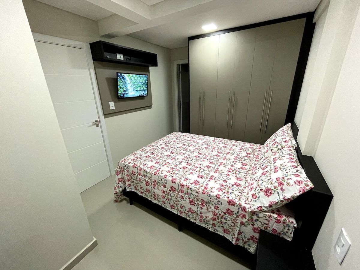 A bedroom with a bed, a television mounted on the wall, and a wardrobe.