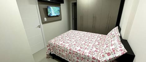 Un dormitorio con una cama, un televisor montado en la pared y un armario.