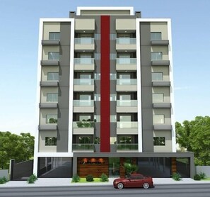 Un edificio moderno de varios pisos con balcones, una franja vertical roja y un coche estacionado adelante.