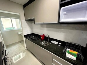 A modern kitchen with a gas stove, stainless steel sink, and a microwave. - Residencial Dinapoli (Foz do Iguaçu)