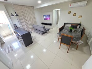 Una sala moderna con comedor, un sofá, una máquina de café y un televisor de pantalla plana en la pared.