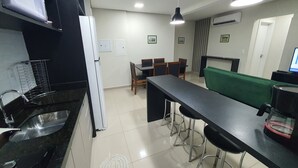 Una cocina moderna con encimera negra, pileta de acero inoxidable y una zona de comedor con sofá verde y sillas de madera.