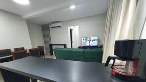 Un comedor moderno con una mesa larga, taburetes de bar, un televisor y una cafetera.