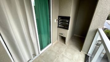 Uma pequena varanda com porta de correr, piso ladrilhado e prateleira fixada na parede.