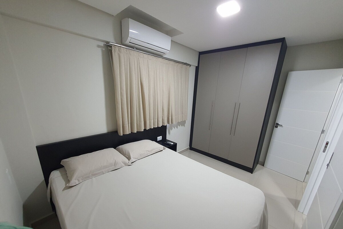 Una habitación de hotel con una cama, un aire acondicionado, un armario y una puerta.