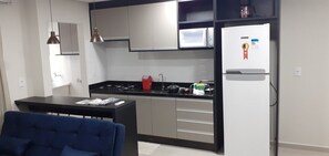 Cocina compacta con estufa a gas, microondas y refrigerador, una mesa de comedor con sillas y un sofá azul.