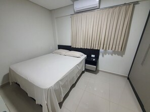 Una habitación de hotel con cama, mesita de noche, toma de corriente y ventana con cortinas.
