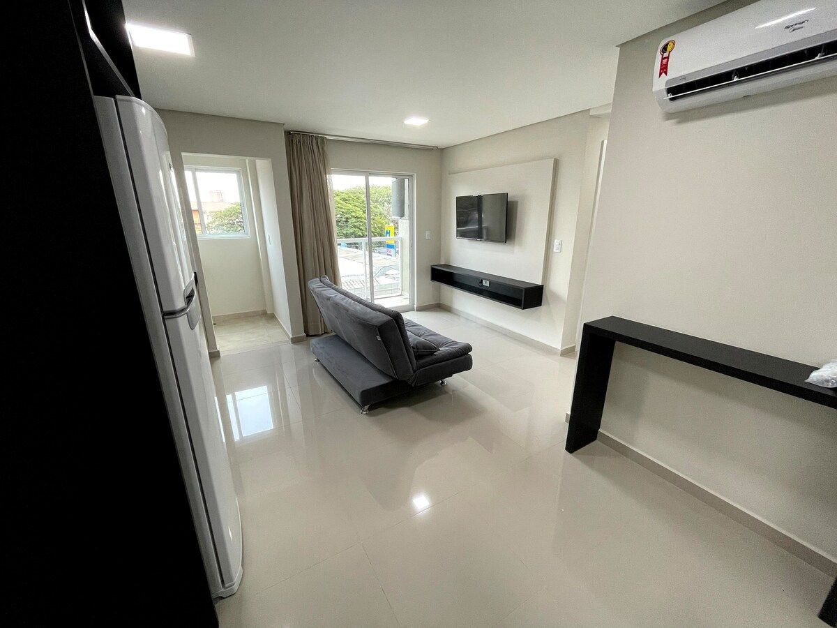A modern living room with a sofa, a flat-screen TV, and a black shelf unit.