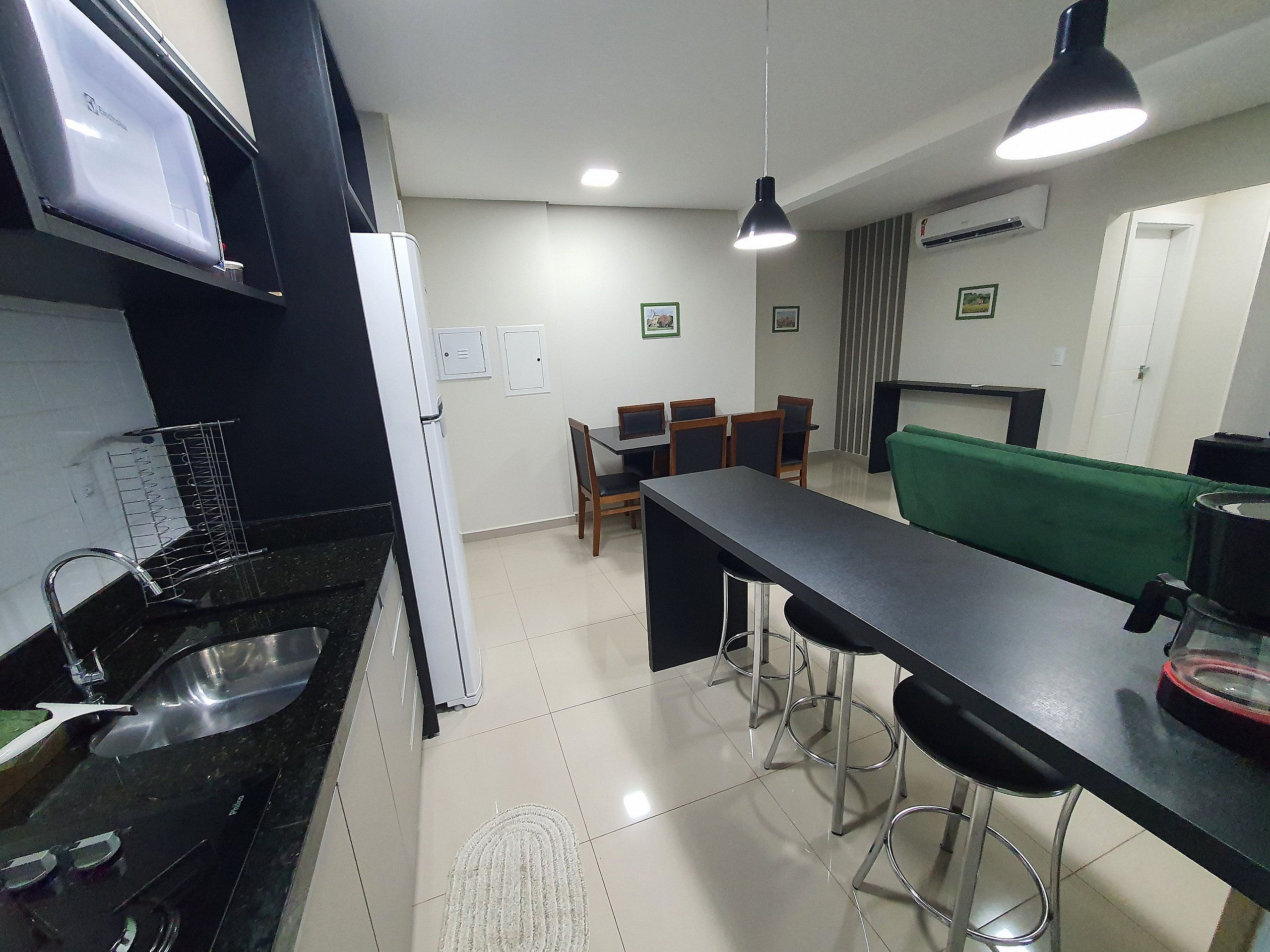 Cozinha compacta com geladeira, pia e área de refeições com cadeiras e mesa.