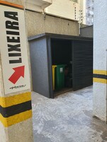 Esquina de un edificio con un cartel que dice 'LIXEIRA' y un contenedor verde para reciclaje.