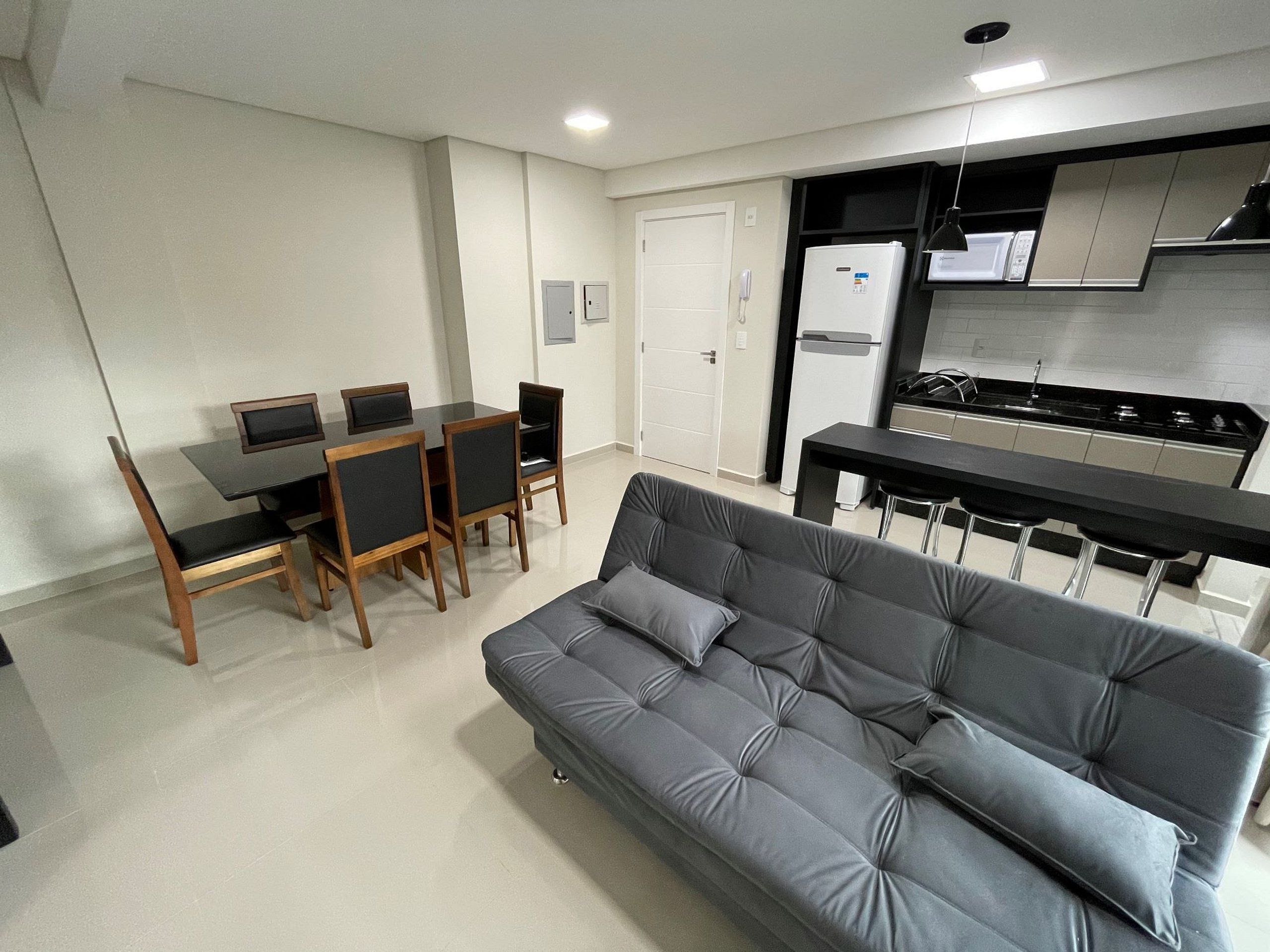 Un espacio habitable compacto con sofá, mesa de comedor, sillas, kitchenette y una puerta.