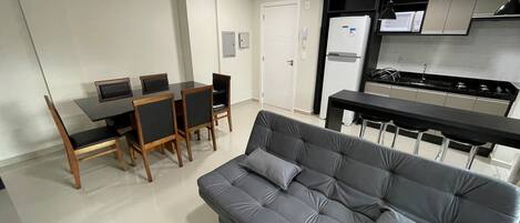 Un espacio habitable compacto con sofá, mesa de comedor, sillas, kitchenette y una puerta.