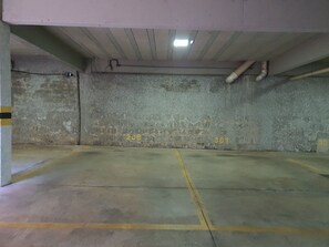 Un garaje para estacionamiento con pisos y paredes de concreto, espacios delimitados y tuberías expuestas.