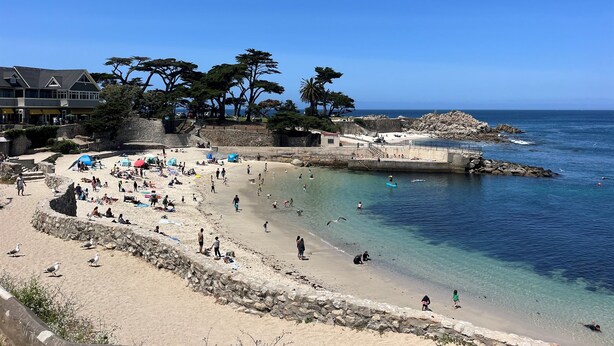 A beach with a stone wall, clear blue water, and a few people. - Romantic Carmel Cottage: Ocean & Country Views (Carmel)