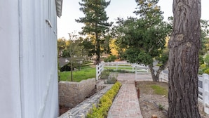 A stone pathway leading to a white fence, surrounded by greenery and trees. - Romantic Carmel Cottage: Ocean & Country Views (Carmel)