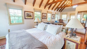 A bedroom with a large bed, wooden beams, and multiple windows. - Romantic Carmel Cottage: Ocean & Country Views (Carmel)